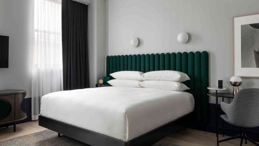 Double-size bed with green headrest and a table and a chair lying just beside the bed